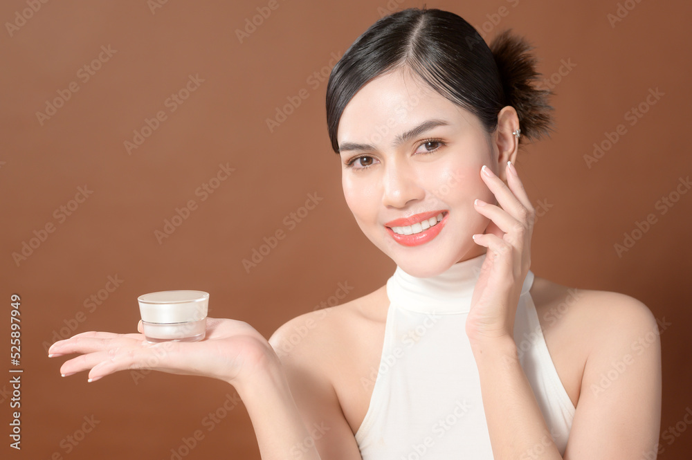 A young woman with beautiful face is holding cream , using cream of her face , beauty skin care concept A young woman with beautiful face is holding cream , using cream of her face , beauty skin care concept