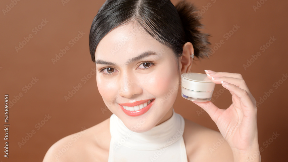 A young woman with beautiful face is holding cream , using cream of her face , beauty skin care concept A young woman with beautiful face is holding cream , using cream of her face , beauty skin care concept