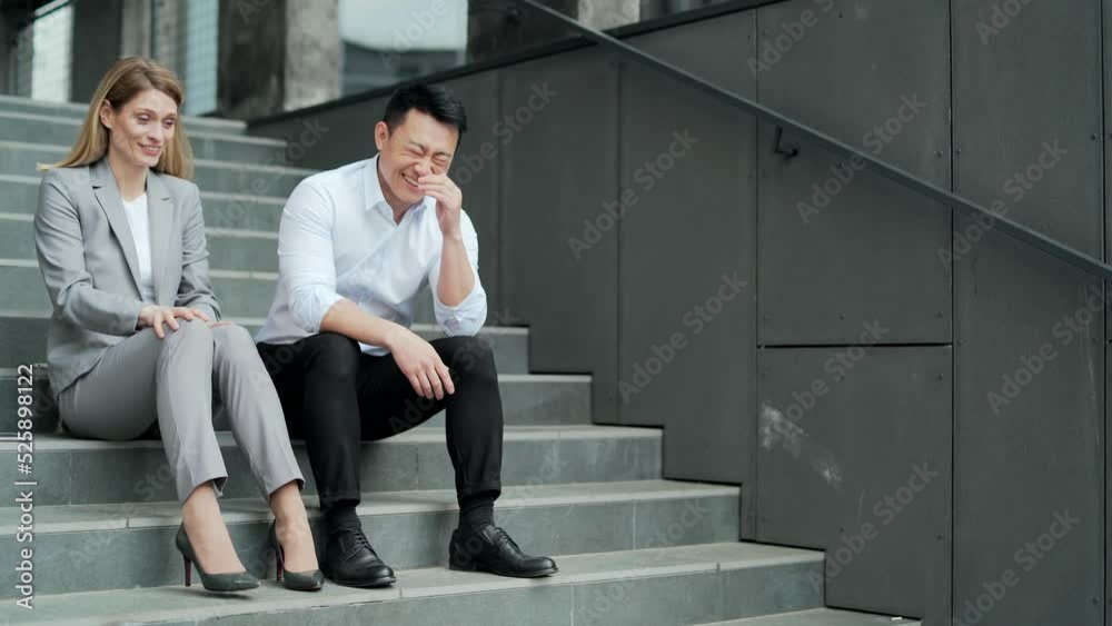 cheerful friends employees talking laughing together sitting on the stairs near the office building together during a break. Funny colleagues business man and woman outside. Friendship of workers