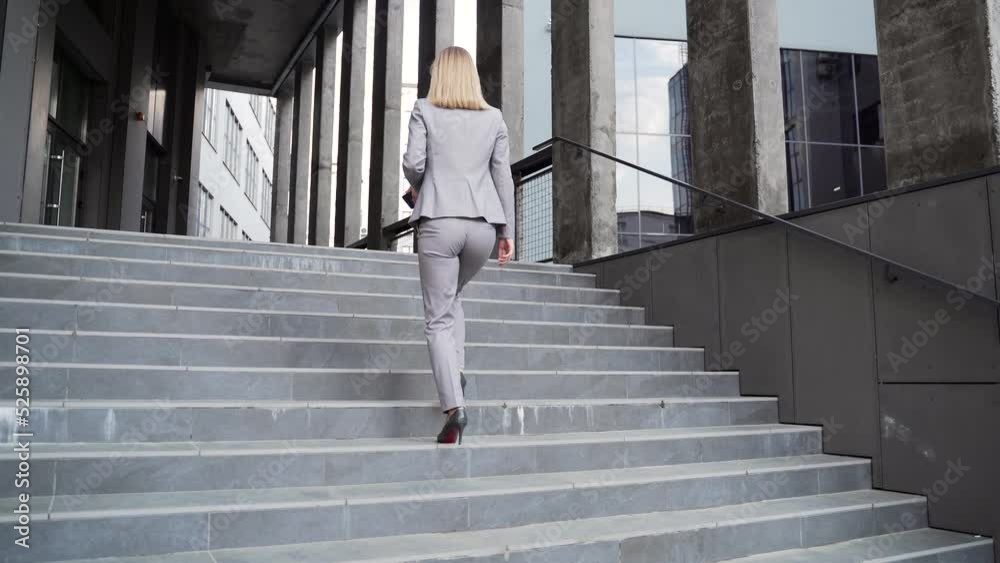 rear view Business woman employee climbs up stairs the step. To office center outside. Businesswoman goes to work. female office worker in a formal suit walks ascending staircase modern urban building rear view Business woman employee climbs up stairs the step. To office center outside. Businesswoman goes to work. female office worker in a formal suit walks ascending staircase modern urban building