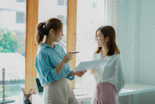 Two Asian women talk, discuss, work on the new start-up project idea. Analyze financial graphs, marketing plans and office investments.