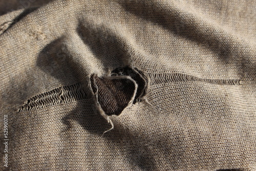 Hole in clothing or piece of cloth. Concept for tattered or torn clothes, mending clothes, repairing clothing, fabric tears, small hole, ripped jumper
