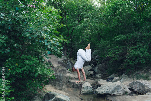 a young guy is doing yoga in nature  performing a handstand.