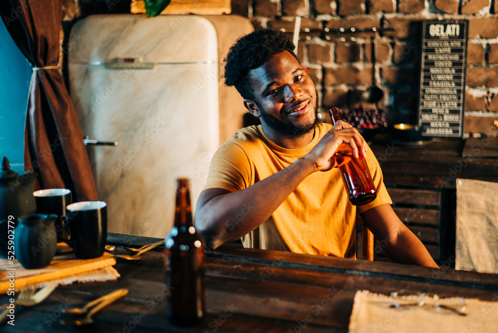 Shot of attractive african young happy smiling man drinking beer bottle in the bar close up portrait.