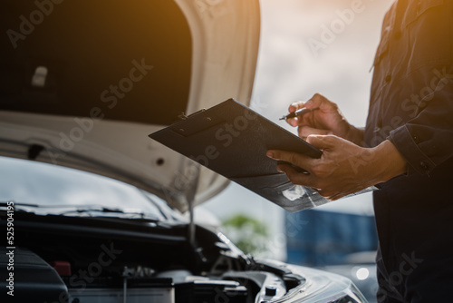 Male mechanic is checking the car maintenance lists for maintenance and fixing the car.