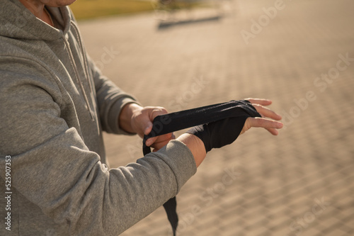 Caucasian man in hoodie bandaging his hands before boxing class outdoors.