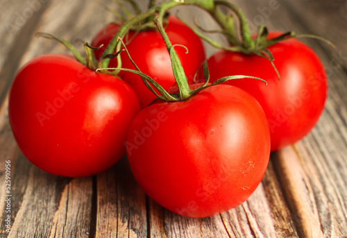 Four whole fresh raw red tomatoes with green twigs on a wooden background, close-up