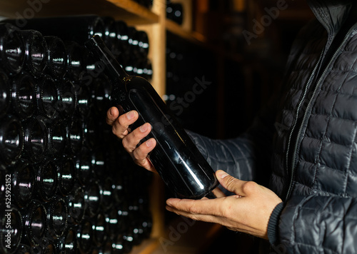 Man in the wine cellar with bottles in background drinking and tasting wine.