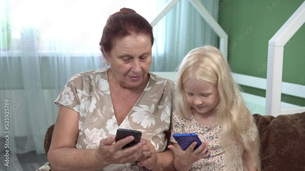 Grandmother and child granddaughter use smartphones together. Girl and grandmother with mobile phones Grandmother and child granddaughter use smartphones together. Girl and grandmother with mobile phones