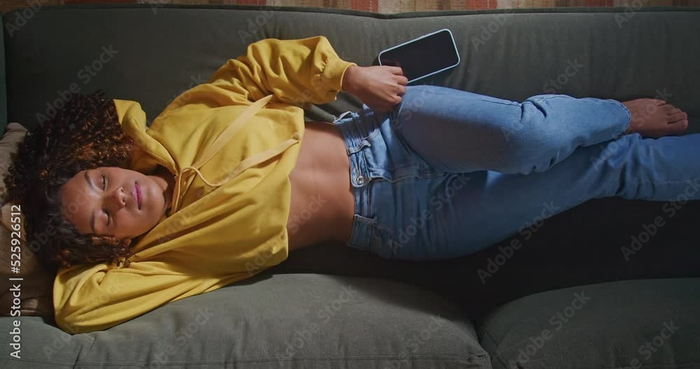 One hispanic black girl putting cellphone away. From above angle of an African American young woman resting on sofa. Restful person relaxing in the evening at living room home napping One hispanic black girl putting cellphone away. From above angle of an African American young woman resting on sofa. Restful person relaxing in the evening at living room home napping
