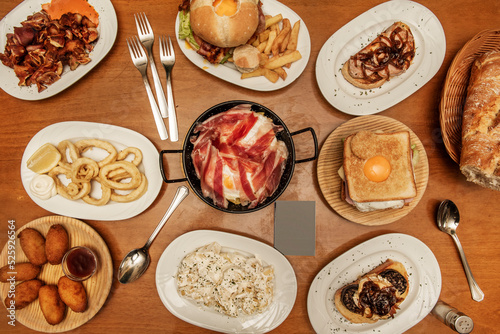 Plates and trays of typical recipes of Spanish gastronomy with croquette tapas, grilled ear, alioli potatoes, Andalusian squid, toast, sandwich with fried egg, hamburgers and scrambled eggs with ham