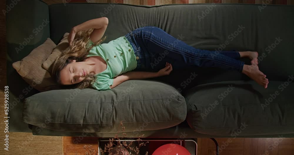 One young woman relaxing on couch. From above angle of a restful girl in her 20s lying on sofa in the living room
