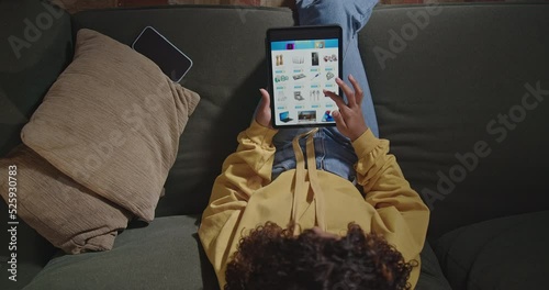 Woman holds tablet surfs online shopping sites. Girl sitting on couch browsing online retail store searching for product to buy
