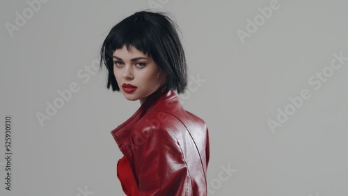 Woman professional fashion model posing in a stylish red coat and red shirt in a black wig in the studio on a white background. Professional fashion posing for the camera