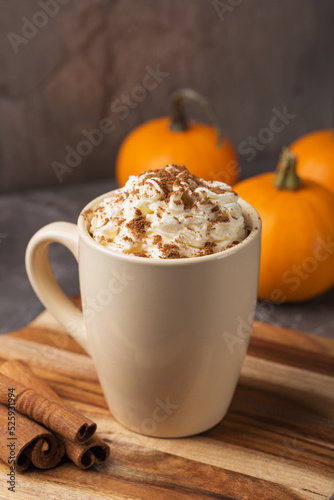 Autumn pumpkin spice latte with cream in mug on dark table. Traditional Coffee Drink for Autumn Holidays. A table decorated with pumpkins. Thanksgiving. Fall time. Vertical orientation. 