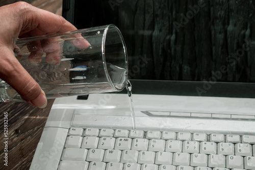 Water from a glass pours onto a laptop keyboard. Computer damaged by negligence