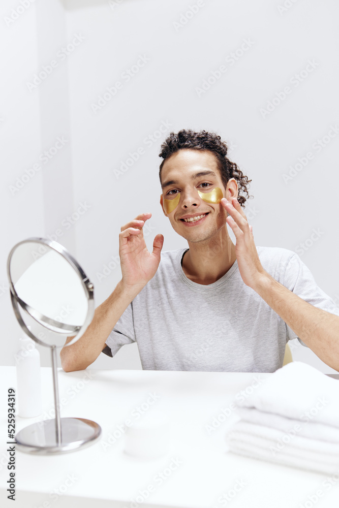 handsome guy in a white T-shirt sits at a table with a mirror and a towel face patches light background handsome guy in a white T-shirt sits at a table with a mirror and a towel face patches light background