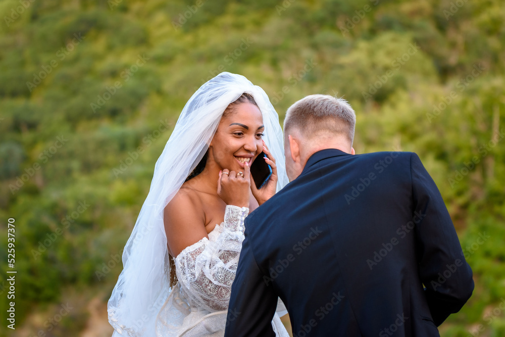 A black bride accepts congratulations on the phone and looks happily at her white husband