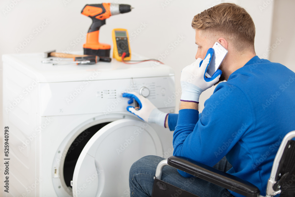 disabled man repairing tumble-dryer making call on smartphone disabled man repairing tumble-dryer making call on smartphone