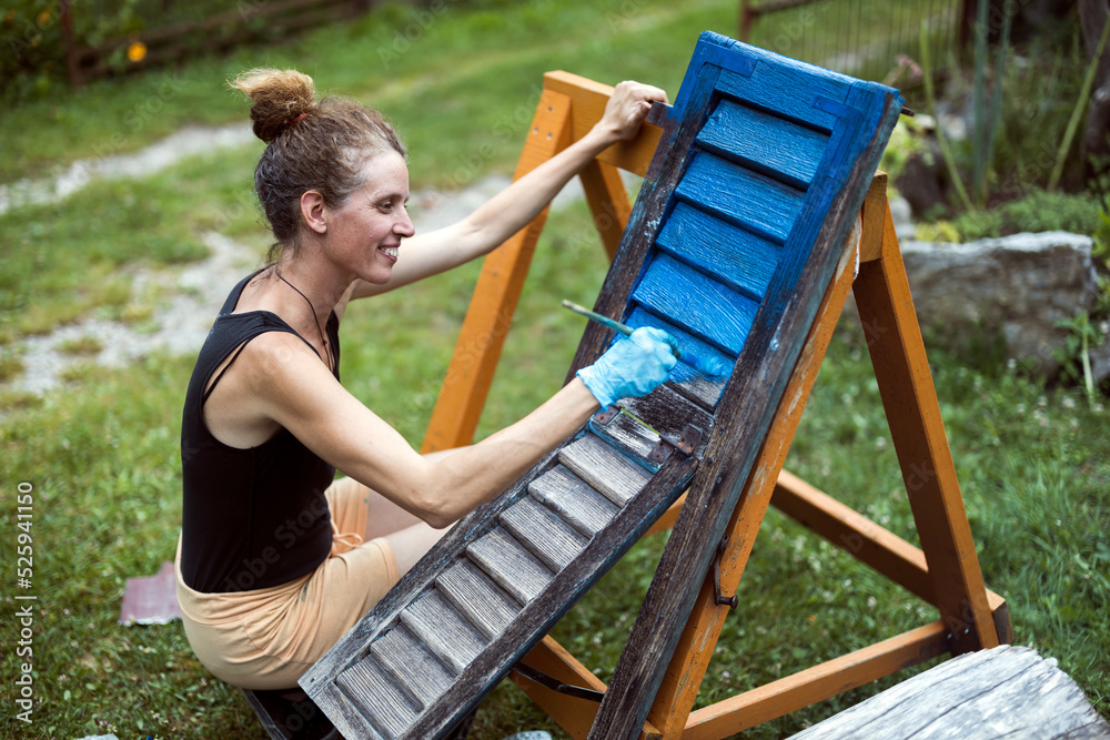 Woman painter in Renovation of old Wooden Windows painting them in Blue Colour