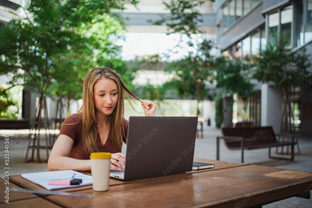 Shot of pupil girl reading a document on her laptop while she is at the university campus Shot of pupil girl reading a document on her laptop while she is at the university campus