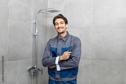 Portrait of handsome smiling plumber fixing shower in the bathroom. Cheerful repairman standing and holding screwdriver in maintenance and service concept