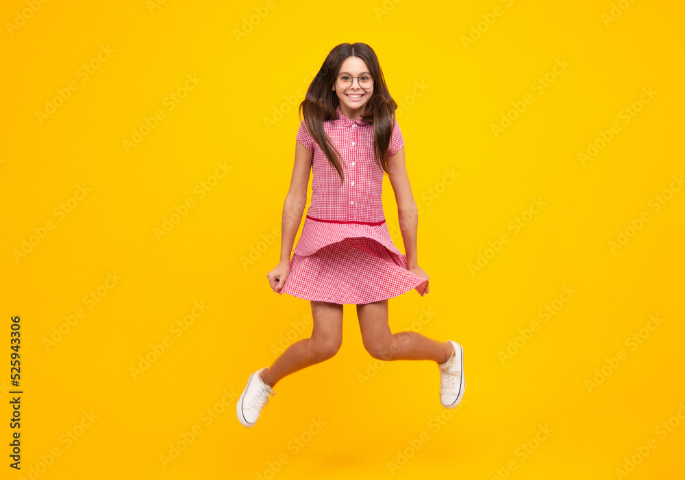 Full length cheerful teenager kid jump enjoy rejoice win isolated on yellow background. Small child girl in summer dress jumping.