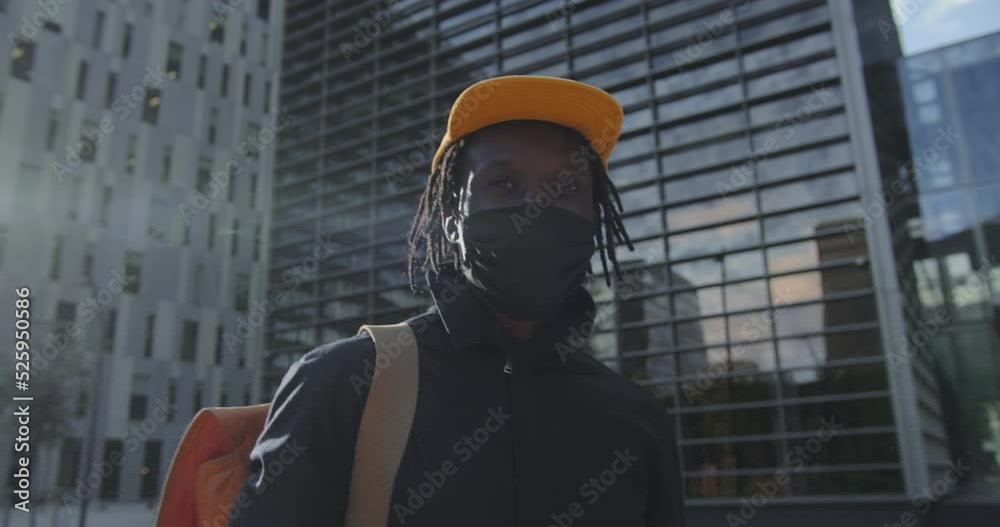 Portrait young black man wearing wearing a medical coronavirus protective mask and standing outside in street looking at camera. African American person portrait. High quality 4k footage Portrait young black man wearing wearing a medical coronavirus protective mask and standing outside in street looking at camera. African American person portrait. High quality 4k footage