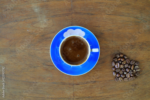 Close-up and top view of hot black coffee in blue coffee cup and roasted Thai coffee beans on wooden background. photo