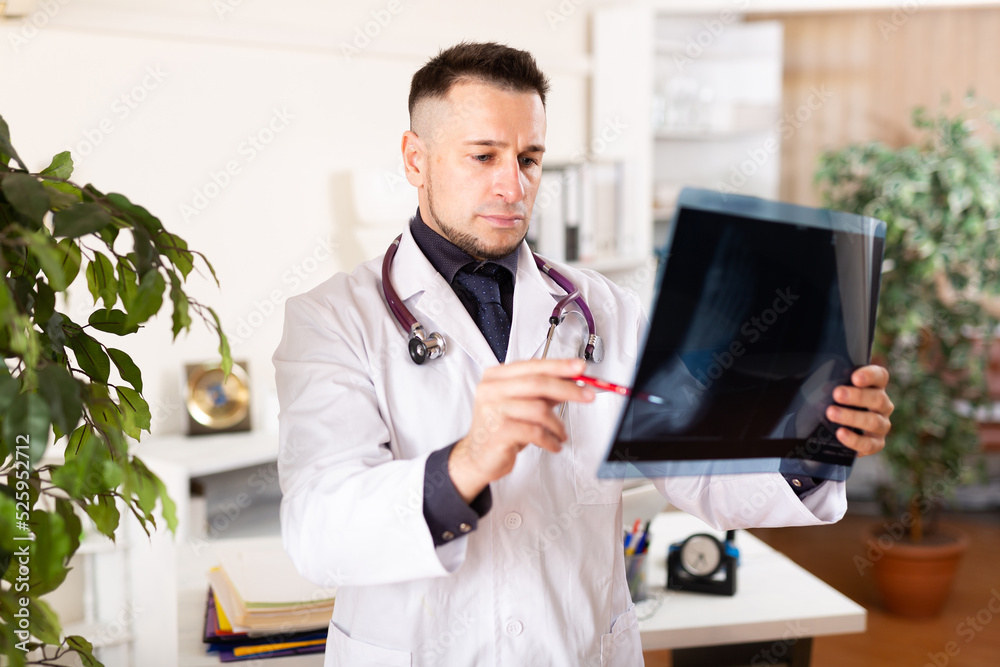 Fototapeta premium European man physician standing in office and analyzing roentgenogram.
