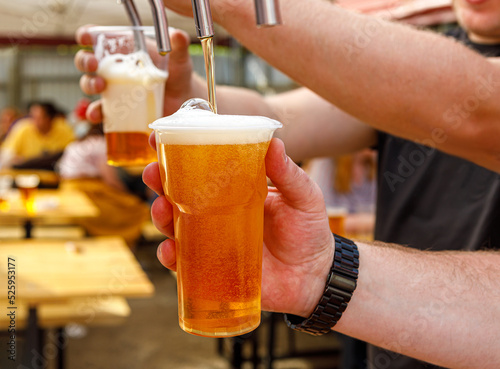 In the hand of a plastic glass with beer, the process of pouring from the tap.
