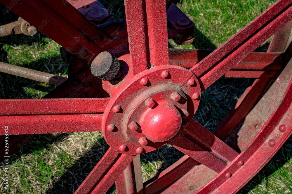 An old red wagon wheel on an antique tractor. The oil cap is covered in muck and dirt. Each wheel needs to be well-oiled to keep it moving freely.