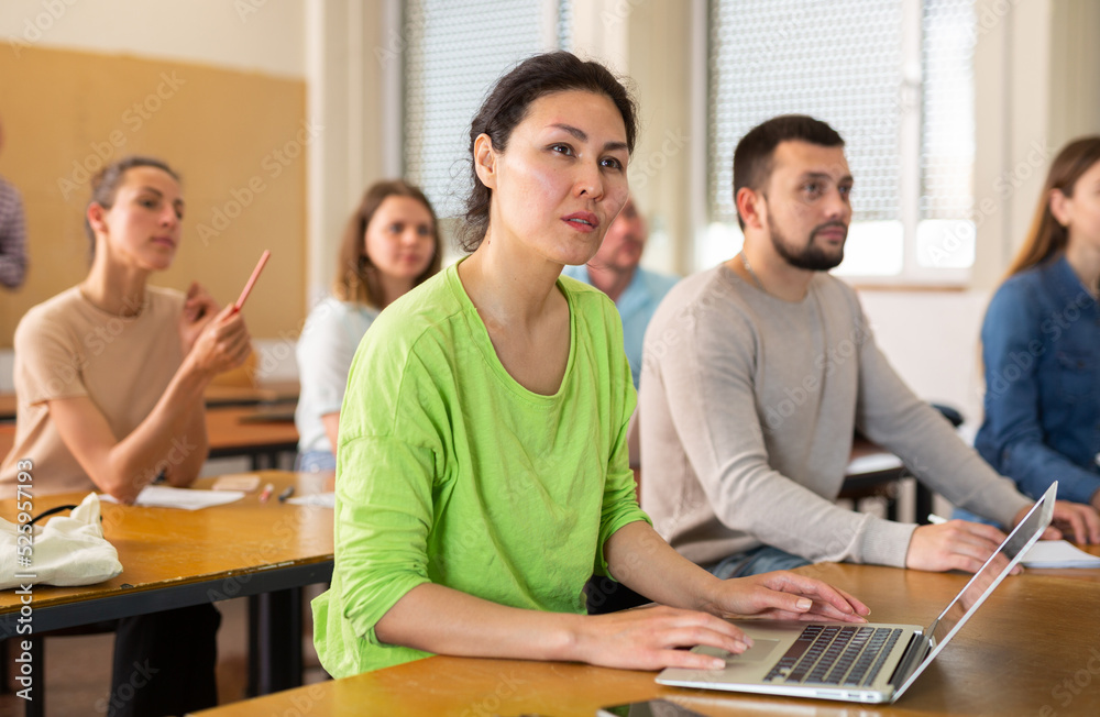 Asian girl is a student engaged on a laptop during classes, studying in a university auditorium with a group