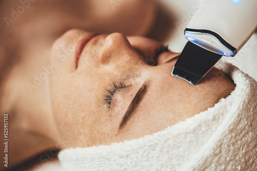 Caucasian freckled woman receiving face cavitation procedure at spa salon. Professional peeling hardware. Electric spa equipment. Medicine patient device photo