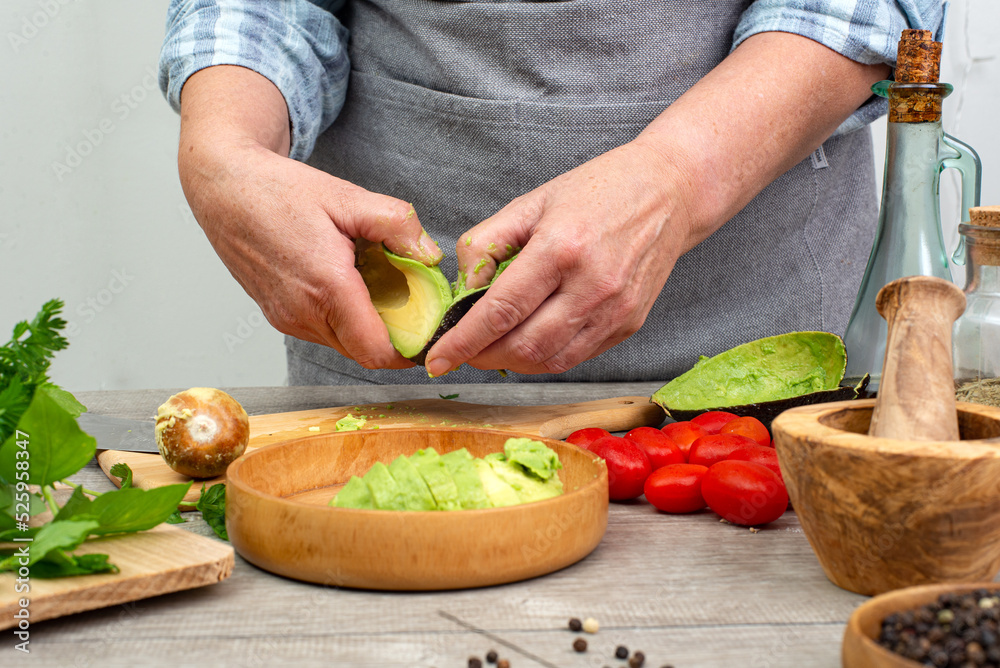 woman's hands preparing avocado to serve. Kitchen table with vegetables and spices