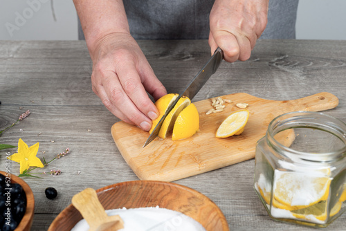 woman's hands cut lemon with a knife on a cutting board. Preparing for canning.