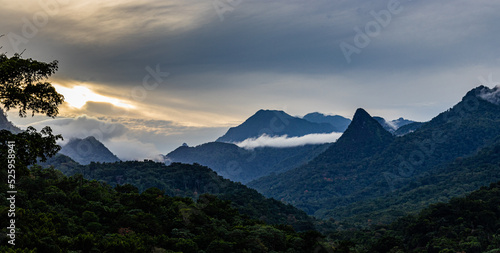 Fotografia horizontal do pôr do sol numa floresta, onde se vê as montanhas e as nuvens, uma paisagem absorvente e icónica de São Tomé e Principe