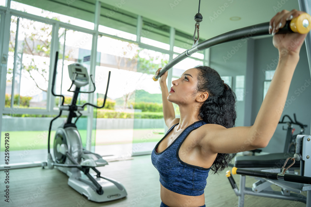 Fototapeta premium beautiful muscular fit woman exercising building muscles. Muscular athletic female bodybuilder pulled on sports simulator.