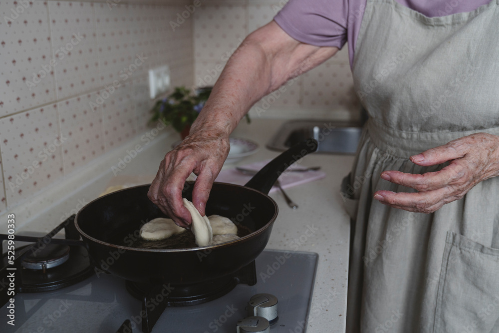 The hands of an elderly woman spread the pies on a frying pan to fry.