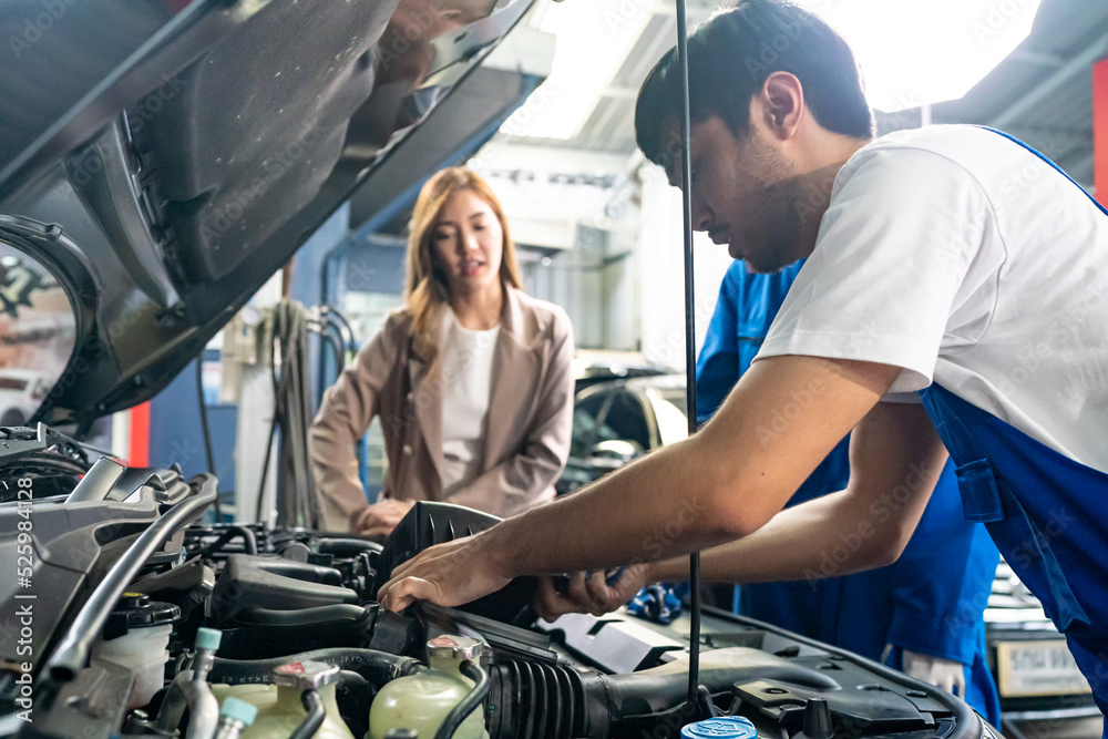 Male car operator wearing blue overalls, gloves working under the hood of car and checking attentively serviceability of engine at repair garage. Concept of car maintenance Male car operator wearing blue overalls, gloves working under the hood of car and checking attentively serviceability of engine at repair garage. Concept of car maintenance