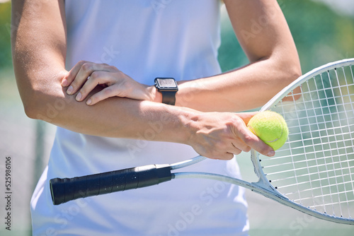 Sports, arm pain and tennis player with a racket and ball standing on a court during for a match. Closeup of a health, strong and professional athlete with equipment touching a medical elbow injury. photo