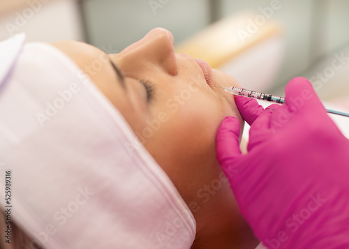 Side view of young woman getting beauty collagen injection. Cosmetologist making anti-wrinkle procedure in pink gloves.