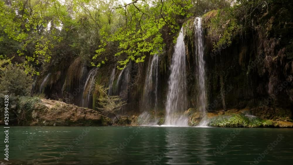 Time lapse shot of Kursunlu Waterfall, many rather small water flows at spring season, dim light in shadow of the trees. Green colour of pond water Time lapse shot of Kursunlu Waterfall, many rather small water flows at spring season, dim light in shadow of the trees. Green colour of pond water