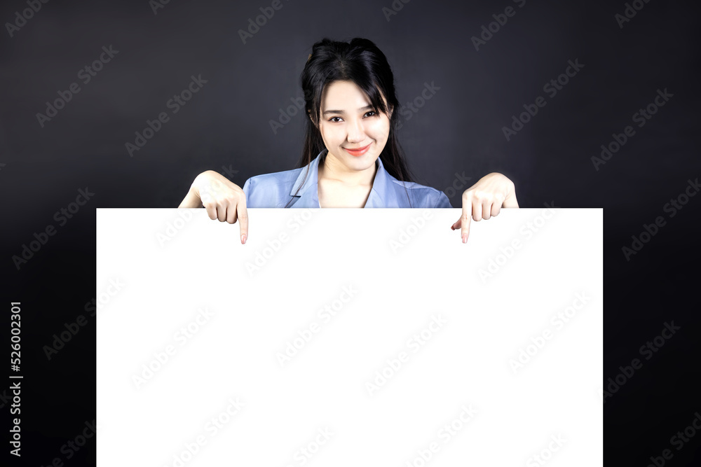 Beautiful Asian woman smiling happily and pointing her finger down at blank white space sign. Blank banner, on gray background. presentation, use for advertising, product brand. Beautiful Asian woman smiling happily and pointing her finger down at blank white space sign. Blank banner, on gray background. presentation, use for advertising, product brand.