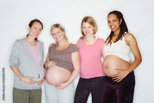 Pregnant, mother and friends with women in studio against a white background feeling happy with a smile. Pregnancy, health and wellness with positive female parents holding their abdomen together