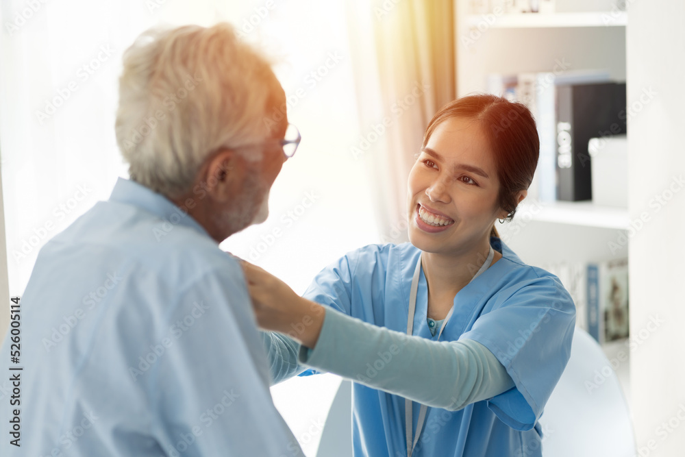 Young female nurse caring senior man sitting in room at hospital. Caring Asian nurse taking care of elderly man in room at nursing home. People and health care concept