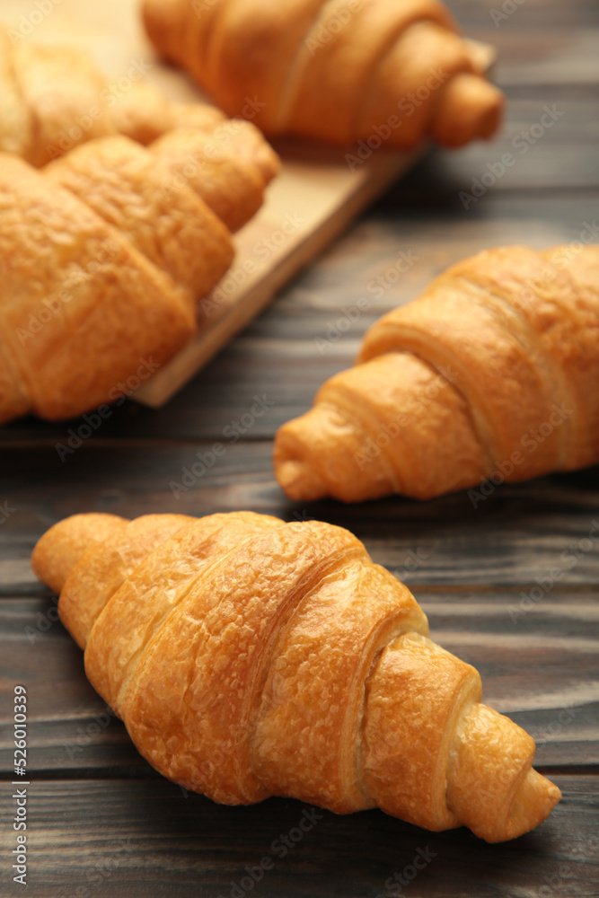 Freshly baked croissants on wooden cutting board on brown background. Vertical photo.