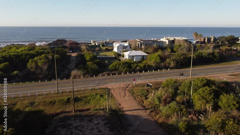 Aerial view of driving motorbike and car on road at sunset and ocean in background - Punta del Este,Uruguay