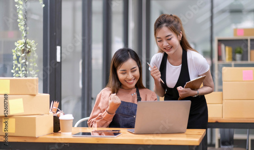 Two Young Asian women are happy and excited after a new order from SME customer, commercial checking, online marketing, Entrepreneur packing boxes, SME sellers, and freelance online sales concept,