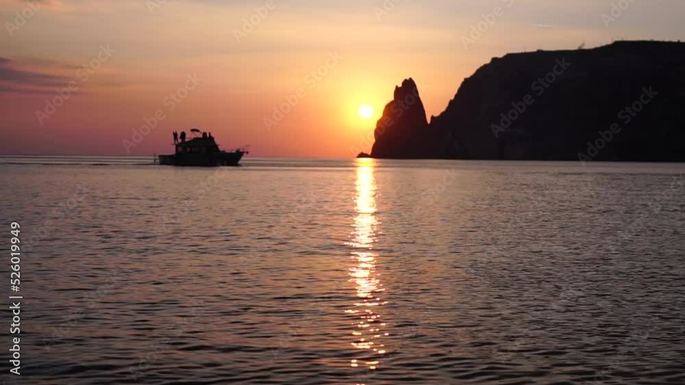 A red burning sunset with the silhouette of a cliff over the sea. Abstract nature summer or spring ocean sea background. Small waves on golden warm water surface with bokeh lights from sun. A red burning sunset with the silhouette of a cliff over the sea. Abstract nature summer or spring ocean sea background. Small waves on golden warm water surface with bokeh lights from sun.